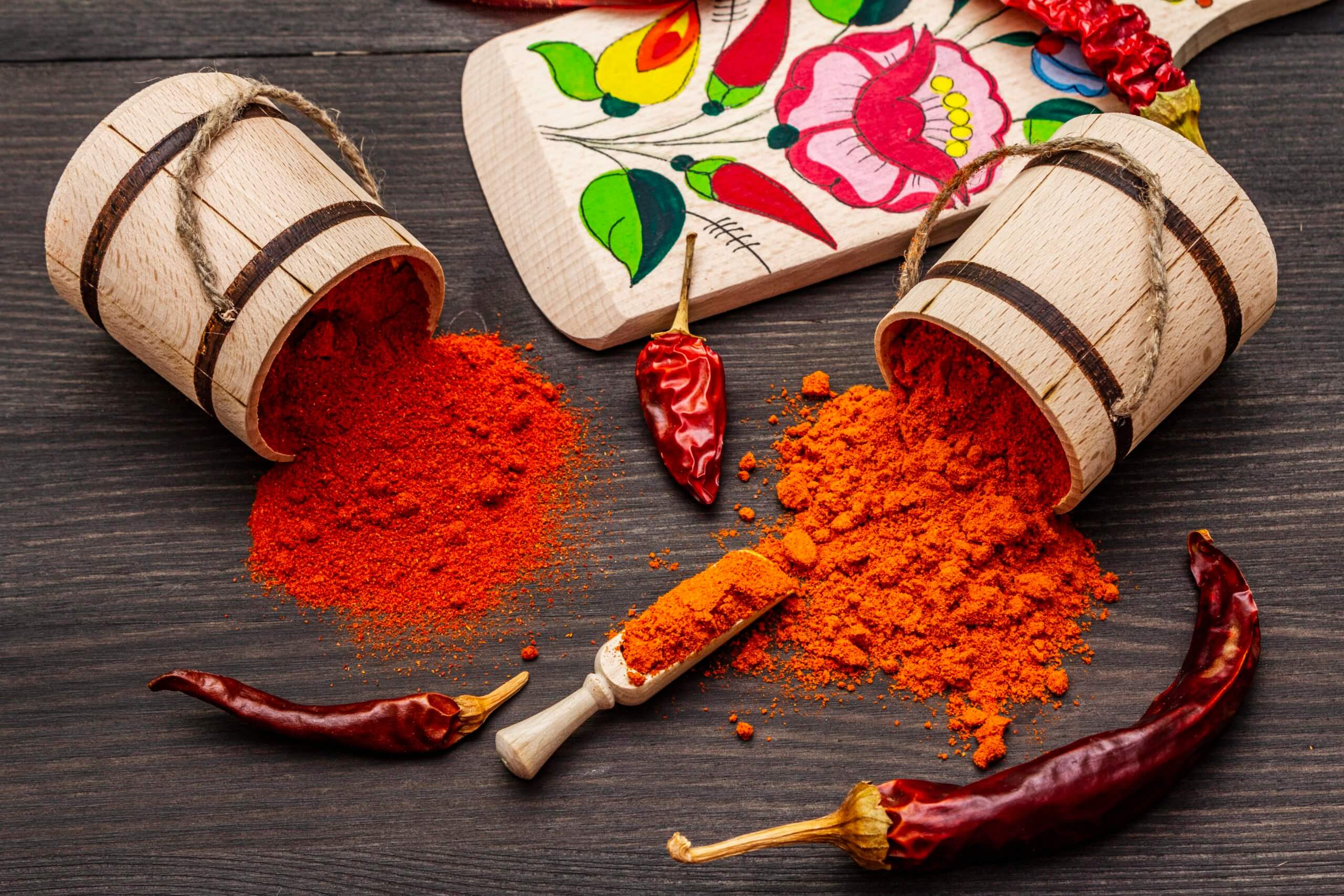 Magyar (Hungarian) red sweet and hot paprika powder. Traditional pattern on a cutting board, different varieties of dry pepper. Black wooden background